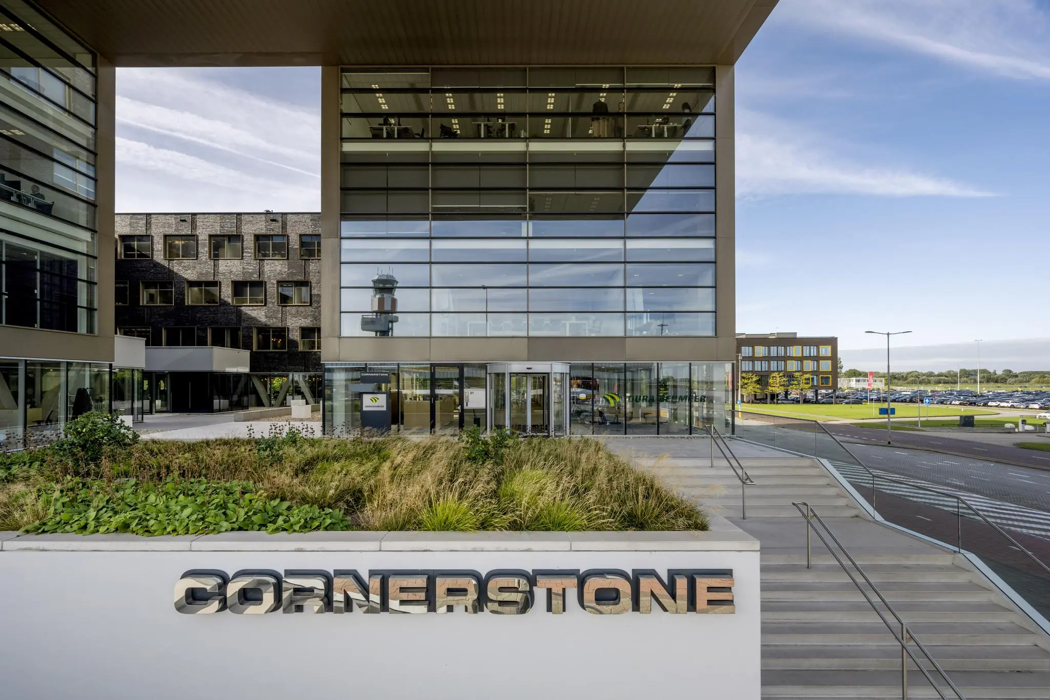 Modern kantoorgebouw Cornerstone aan het Airportplein in Rotterdam met zicht op de hoofdingang en verkeerstoren op de achtergrond.